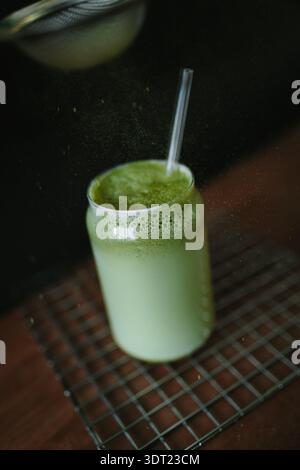 A creamy matcha latte in a transparent glass with a straw sits on a cooling rack. The green tea froth adds a vibrant touch, offering a refreshing visu Stock Photo