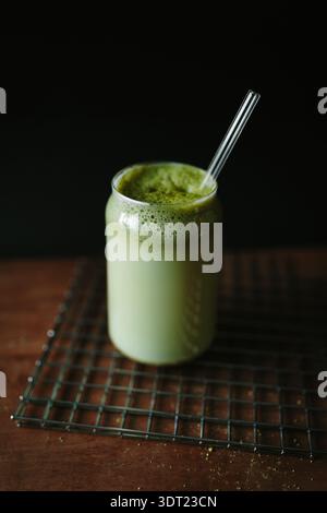 A creamy matcha latte in a transparent glass with a straw sits on a cooling rack. The green tea froth adds a vibrant touch, offering a refreshing visu Stock Photo