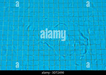 A vivid blue tiled surface underwater, displaying seamless tiles disturbed by slight water ripples. The grid pattern forms a captivating geometric des Stock Photo
