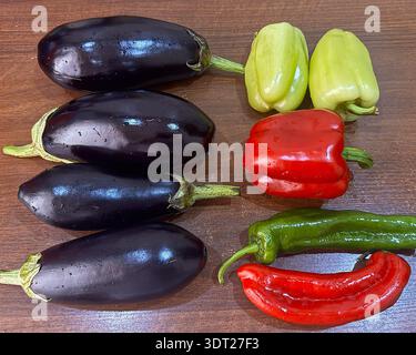 Fresh Whole Eggplants and Colorful Bell Peppers on Wooden Surface Stock Photo