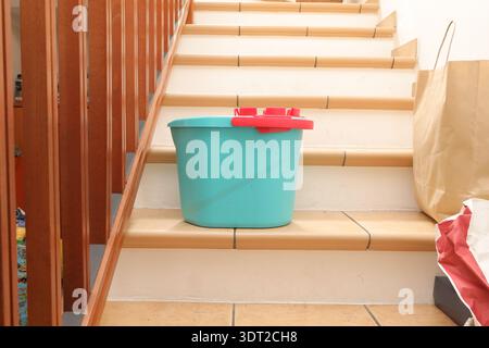 Blue bucket with red lid on stairs next to brown paper bags in a home environment Stock Photo