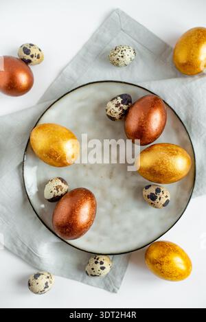 Golden and bronze Easter eggs in a grey plate on a linen napkin on a white background Stock Photo
