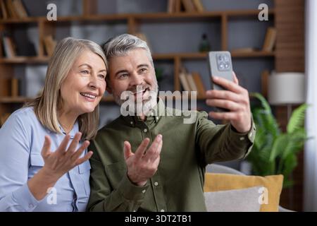 Senior couple communicating with family and friends remotely using a smartphone application for a video call, smiling and expressing happiness while staying connected Stock Photo