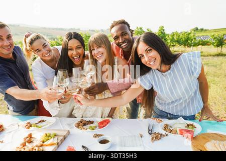 Happy friends having fun drinking white wine and eating together - Multiracial people doing party at summer time in countryside Stock Photo