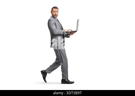 Full length shot of a cheerful professional man walking and using a laptop computer isolated on white background Stock Photo