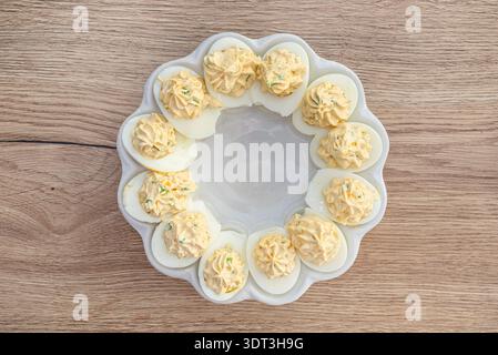 Deviled eggs arranged in a round platter with chives on a wooden surface Stock Photo