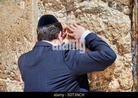 An Orthodox Jew is praying by the Wailing Wall in Jerusalem. The person leans against the stone, showing devotion during the prayer. Stock Photo