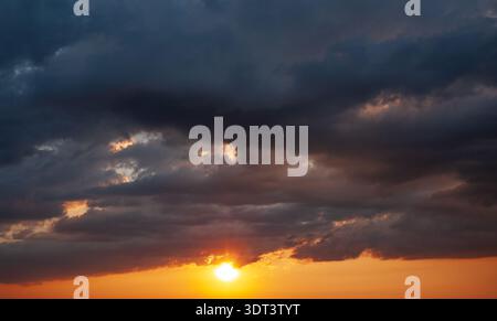 Dramatic dark clouds with sun rays breaking through sunset storm sky Stock Photo