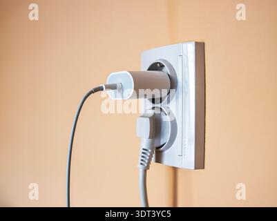 White wall socket with connected power adapter and thick cord in residential interior setting Stock Photo