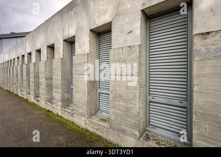 Industrial building exterior featuring a row of concrete windows closed with metal shutters. Perspective view of a modern commercial wall with repeati Stock Photo