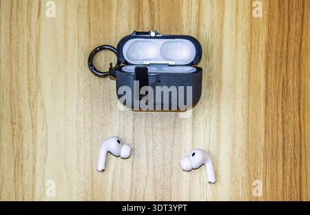 Pair of white AirPods Pro 3 next to open black charging case on wooden surface. Stock Photo