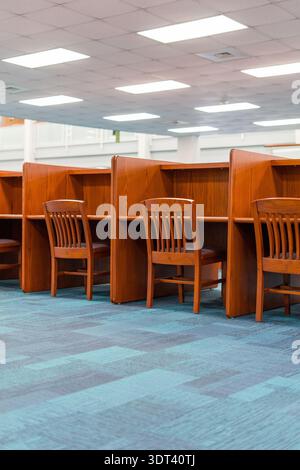 A vertical shot of a row of traditional wooden study desks and chairs in a quiet library or office workspace. The interior features a blue patterned c Stock Photo