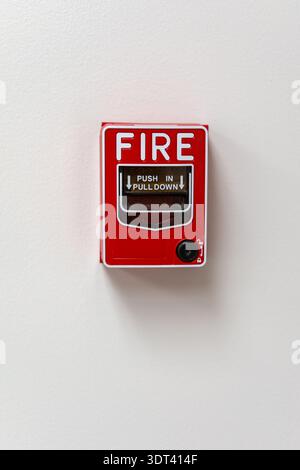 A vertical close-up of a red manual fire alarm pull station mounted on a plain white wall. The device features clear instructions "Push In, Pull Down" Stock Photo