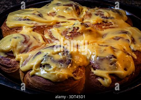 Close-up of freshly baked cinnamon rolls topped with thick yellow frosting, warm and glossy in soft light Stock Photo