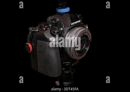 Close-up of Olympus digital camera with M.Zuiko 14–42mm lens mounted on tripod against black background Stock Photo