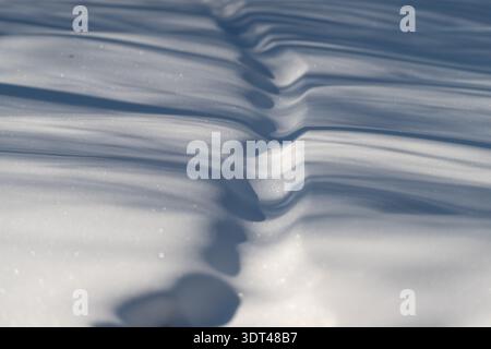 Frozen ripples form scenic waves. Repeated snow ripples generate undulating visuals with sunlight creating shadows and shimmering mountain tops Stock Photo