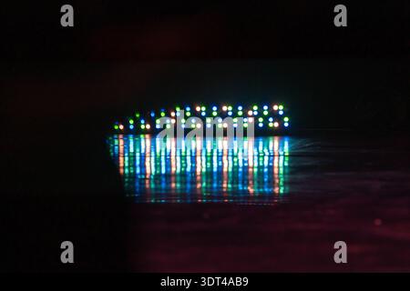 A horizontal row of colorful LED lights creates a bokeh strip and vivid reflection on a wet floor at night, producing an abstract, cinematic mood with Stock Photo