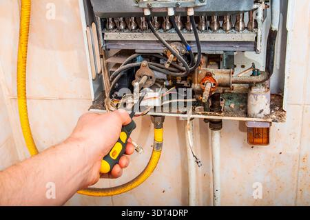 Close-up of a technician's hand working on the intricate wiring and pipes of a malfunctioning gas water heater unit Stock Photo