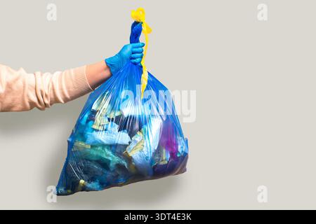 Hand holding full garbage bag on grey background isolated. High quality image Stock Photo