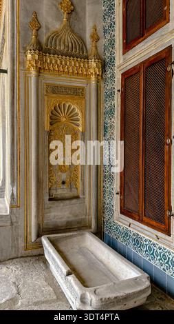 Gilded Ottoman wall fountain with a marble basin and tiled walls inside the Imperial Harem of Topkapi Palace, Istanbul, Turkey. Stock Photo