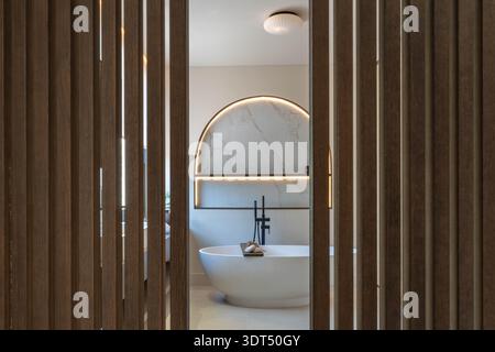 an image through wooden beams of a luxury bathtub and illuminated shelving in luxury mediterranean bathroom Stock Photo