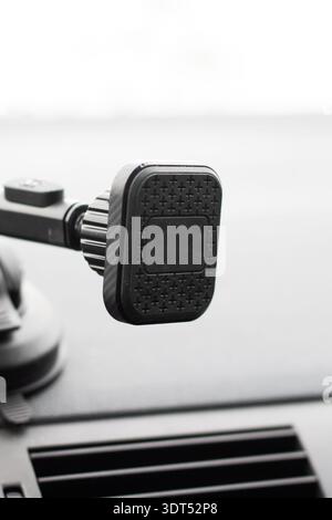 Car dashboard magnetic phone mount with raindrops on black pad, adjustable arm and suction base attached to windshield, Stock Photo