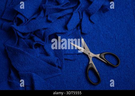 Bright blue wool fabric scraps with metal scissors on a wool background depict sewing leftovers, craft tools, and sustainable textile practices. Stock Photo