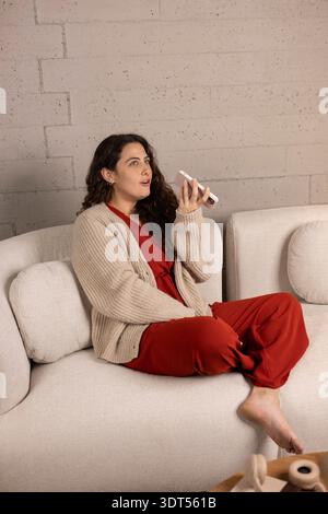 Woman listening to a voice message or speaking into her mobile phone while relaxing Stock Photo