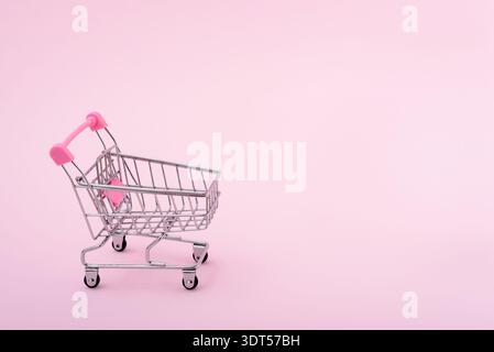 Empty mini metal shopping cart with wheels on a light pink background with copy space for text. Concept shopping in supermarket. Stock Photo
