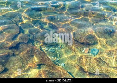 Bright sunlight creates golden caustic patterns on the rocky bottom of clear turquoise sea water. This natural abstract texture Stock Photo