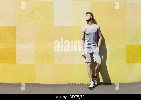 Man Poses Casually Against a Bright Yellow Wall During a Sunny Day in the City Square Stock Photo