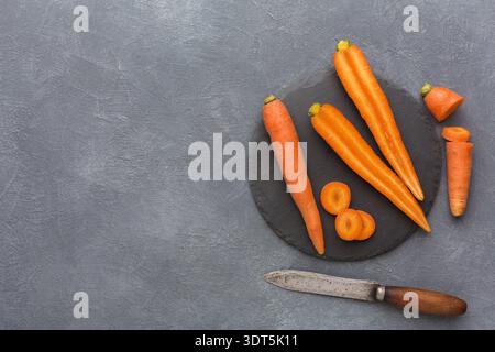 Fresh Carrots Arranged on a Dark Plate With a Knife for Cooking or Preparation on a Gray Surface Stock Photo