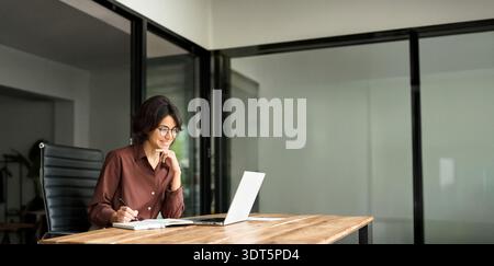 Smiling busy young businesswoman executive looking at laptop in office working. Stock Photo
