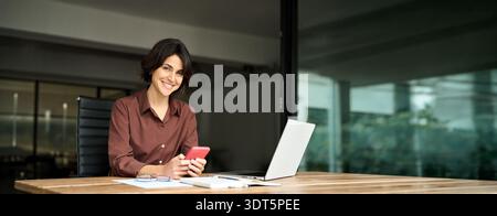 Happy young business woman using smartphone in office. Portrait. Stock Photo