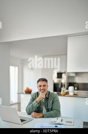 Happy middle aged older man sitting with laptop at home table. Portrait. Stock Photo