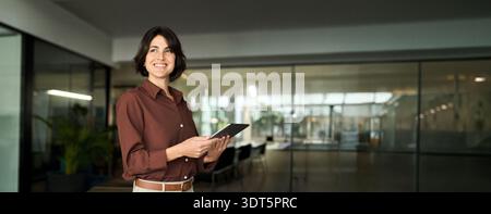 Happy young Hispanic professional business woman using tab standing in office. Stock Photo