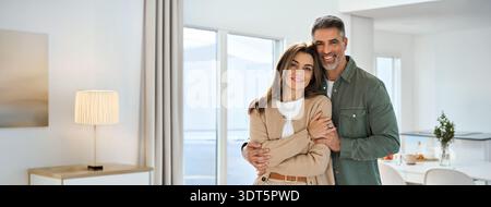 Happy mature couple hugging looking at camera standing in kitchen at home. Stock Photo