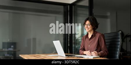 Happy busy young business woman working in office using laptop writing notes. Stock Photo