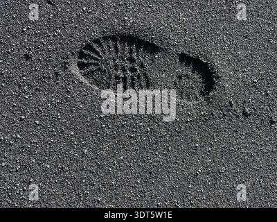 Single footprint pressed into dark volcanic sand, a tiny human trace on a textured black beach Stock Photo