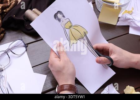 Fashion designer cutting out sketch of outfit at wooden table, closeup Stock Photo