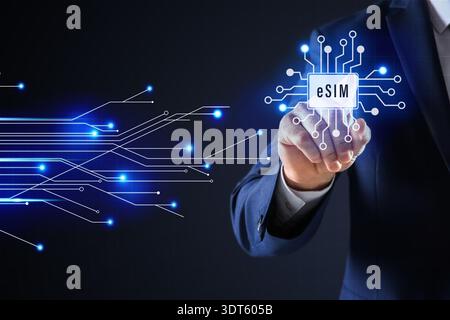 Businessman activating eSIM microchip on virtual screen, closeup. Dark background with circuit board pattern Stock Photo