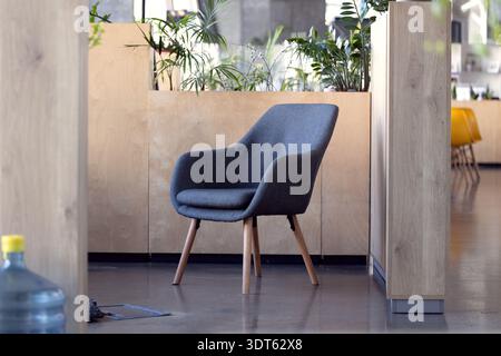 A stylish upholstered chair sits in a bright, modern office environment featuring natural wood accents and lush greenery Stock Photo