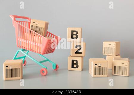 A hand holding three wooden blocks that spell out B2B. The blocks are on a table next to a blue alarm clock Stock Photo