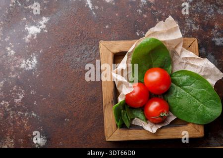 Fresh Tomatoes and Spinach on Brown Surface in a Wooden Plate Stock Photo