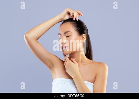 Woman Poses With Hand on Head and Touches Chin in Studio Setting With Gray Backdrop Stock Photo