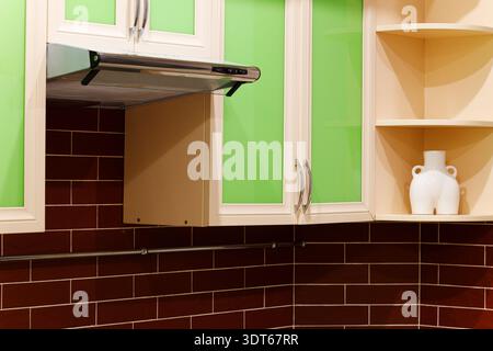 A contemporary kitchen features sleek lime green cabinet doors contrasted with dark brown tiled backsplash and a metallic range hood Stock Photo