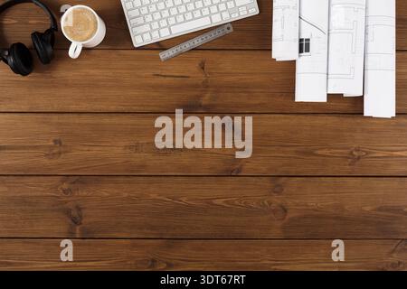 Workspace With Coffee, Keyboard, Headphones, and Architectural Plans on Wooden Table Stock Photo