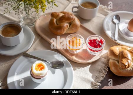 Breakfast with boiled eggs, jam, buns and coffee served on a table in the morning sun, holiday start on Easter, Mother's Day, or on the weekend, selec Stock Photo