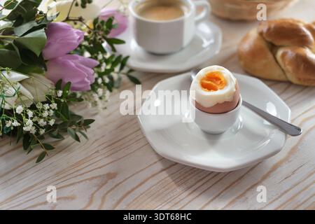 Boiled egg with soft yolk on an wooden breakfast table with buns, coffee and flowers, easter or mothers day, copy space, selected focus, narrow depth Stock Photo
