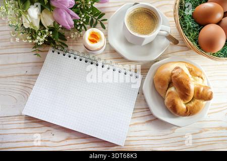 Blank checkered spiral notepad on an Easter table with eggs, rolls, spring flowers, and coffee, mock-up for to-do list, invitation, or save the date, Stock Photo